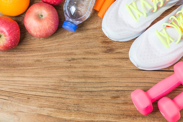 Concepto, botella de agua, mancuernas, zapatos deportivos, smartphone con auriculares y manzanas sobre fondo de madera. Espacio de la copia para el texto. Vista superior