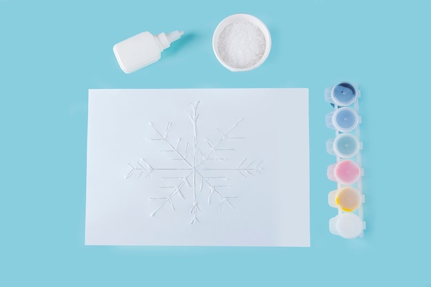 Concepto de bricolaje y creatividad infantil. Instrucciones paso a paso: cómo hacer copos de nieve con pegamento y sal en papel. Paso 3 las manos del niño aplican pegamento al dibujo.