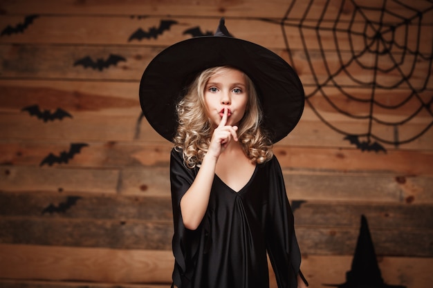 Concepto de la bruja de Halloween - tiro del primer del pequeño niño caucásico de la bruja que lleva a cabo el dedo índice en los labios, pidiendo guardar silencio.