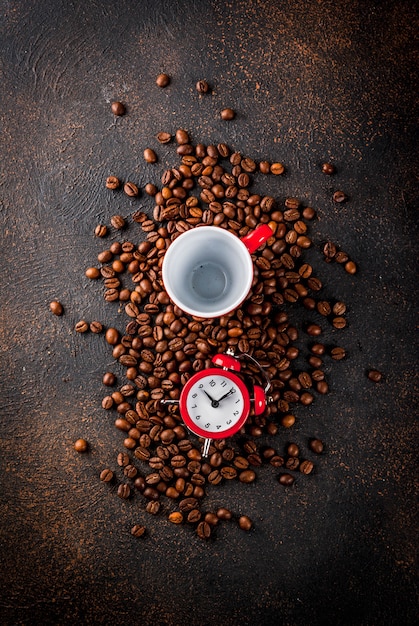 Concepto de un buen comienzo alegre para el día café de la mañana. Fondo oxidado oscuro con granos de café un despertador y una taza de café.