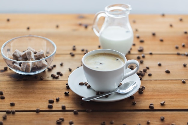 concepto de cafeína, objetos y bebidas - cierre la taza de café y los granos en la mesa de madera