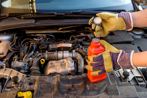 Concepto de cambio de aceite. Mano masculina en guante con botella de aceite y motor de coche de cerca