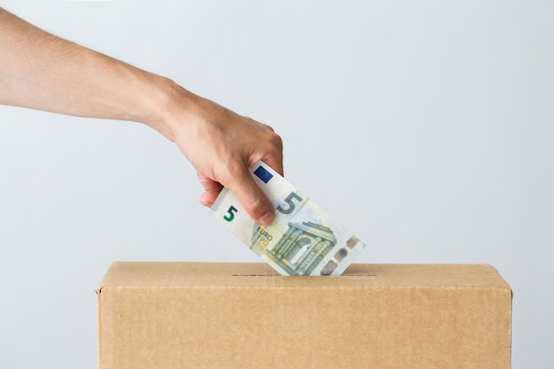 concepto de caridad, finanzas, financiación, inversión y personas - mano masculina poniendo dinero en euros en la caja de donación