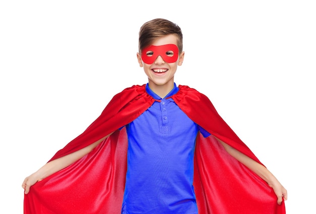 concepto de carnaval, infancia, poder, gesto y personas - niño feliz con capa y máscara de superhéroe rojo