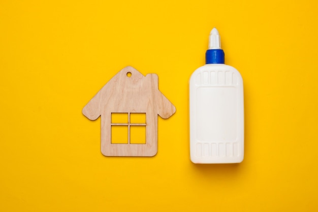 Concepto de casa de bricolaje. Figura mini casa de madera y una botella de pegamento sobre un fondo amarillo. Vista superior