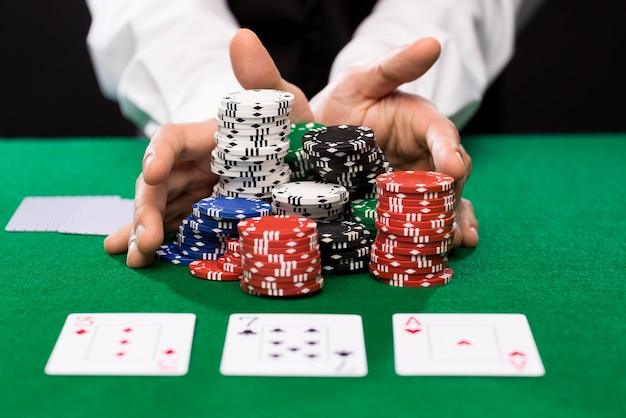 concepto de casino, juegos de azar, póquer, gente y entretenimiento - primer plano del jugador de póquer con cartas y fichas en la mesa de casino verde