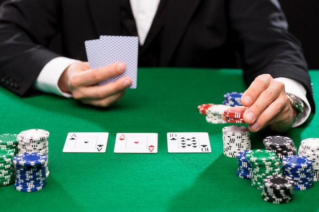 concepto de casino, juegos de azar, póquer, gente y entretenimiento - primer plano del jugador de póquer con cartas y fichas en la mesa de casino verde