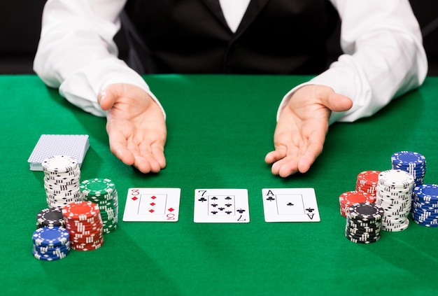 concepto de casino, juegos de azar, póquer, personas y entretenimiento: cierre del crupier de holdem con cartas de juego y fichas en la mesa verde