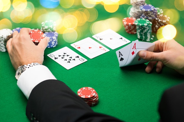 Concepto de casino, juegos de azar, póquer, personas y entretenimiento: cierre de jugador de póquer con cartas y fichas en la mesa de casino verde durante las vacaciones luces de fondo