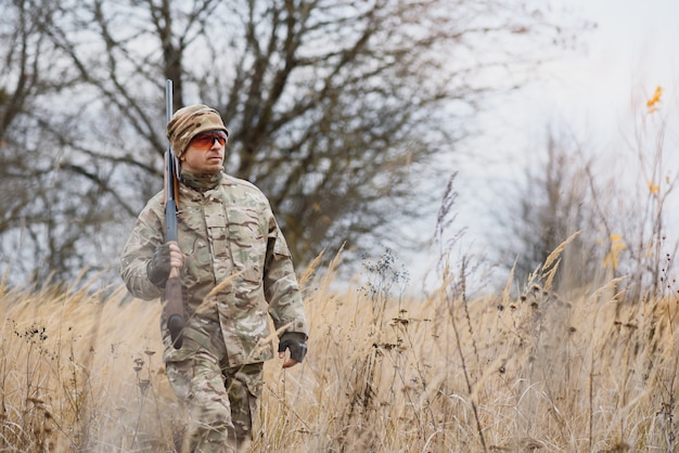 Concepto de caza, guerra, ejército y personas - joven soldado, guardabosques o cazador con pistola caminando en el bosque