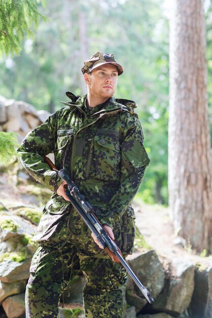 Concepto de caza, guerra, ejército y personas - joven soldado, guardabosques o cazador con pistola caminando en el bosque