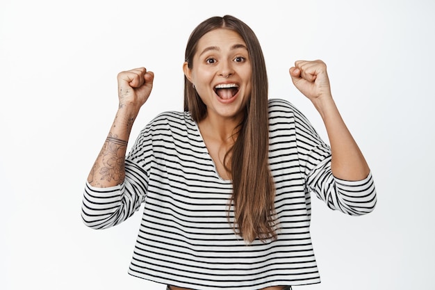 Concepto de celebración. Chica sonriente feliz saltando de la felicidad, levantando las manos y gritando de alegría, ganando y triunfando, fondo blanco.