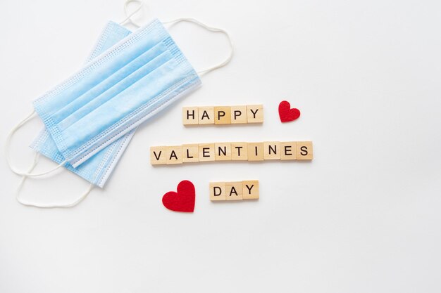 Concepto de celebración del Día de San Valentín Inscripción de madera Feliz Día de San Valentín El 14 de febrero El corazón yace en máscaras médicas la lucha contra el coronavirus