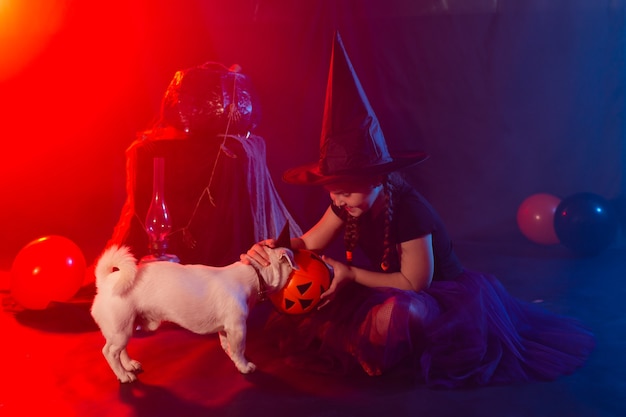 Concepto de celebración y Halloween niña en traje de bruja con calabaza de halloween jugando con