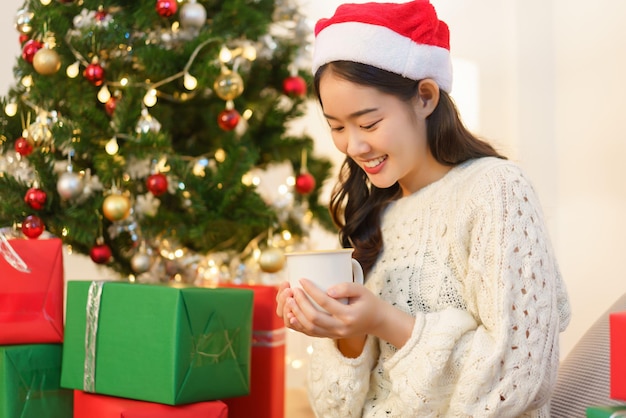 Concepto de celebración de Navidad Mujer asiática sostiene una taza de café y se sienta en una habitación decorada con Navidad