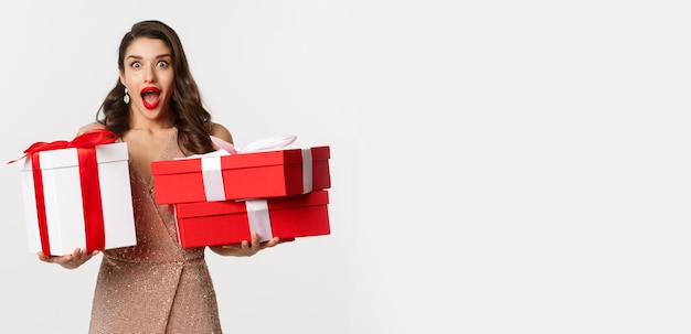 Concepto de celebración navideña emocionada y sorprendida mujer sosteniendo regalos de navidad y sonriendo asombrada