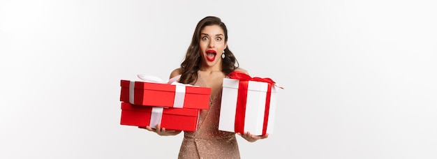 Concepto de celebración navideña emocionada y sorprendida mujer sosteniendo regalos de navidad y sonriendo asombrada