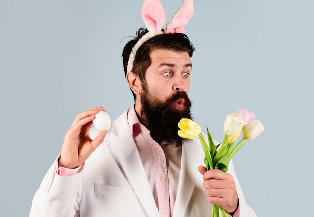 Concepto de celebración de Pascua. Hombre barbudo sorprendido en traje con huevo y flores. Caza de huevos.