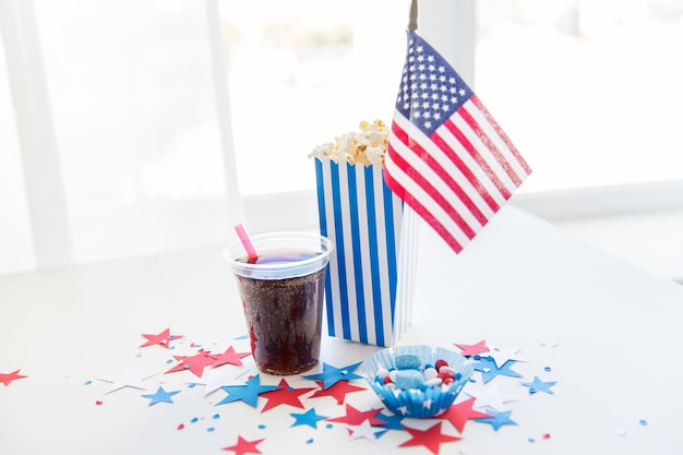 concepto de celebración, patriotismo y vacaciones: cierre de la bandera estadounidense, copa de coca cola, palomitas de maíz y dulces con decoración de confeti de estrellas en la fiesta del 4 de julio el día de la independencia