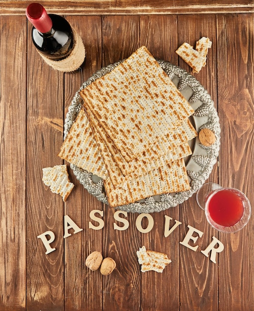 Foto concepto de celebración de pesach festividad judía pesach matzah en plato tradicional de seder con botella de vino tinto copa de vino y nueces sobre fondo de madera y la inscripción pascua