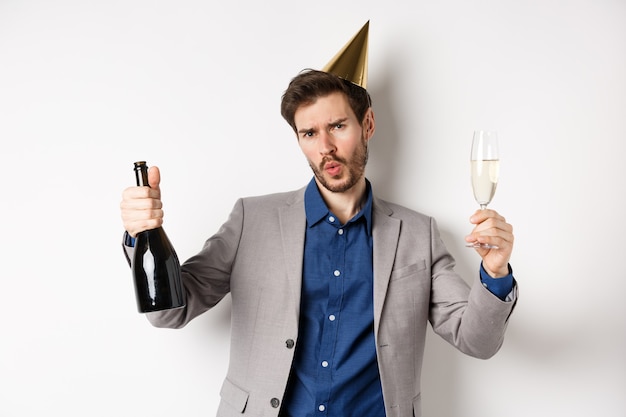 Concepto de celebración y vacaciones. Hombre feliz en traje divirtiéndose en la fiesta, con sombrero de cumpleaños, bailando con champán y bebiendo alcohol.