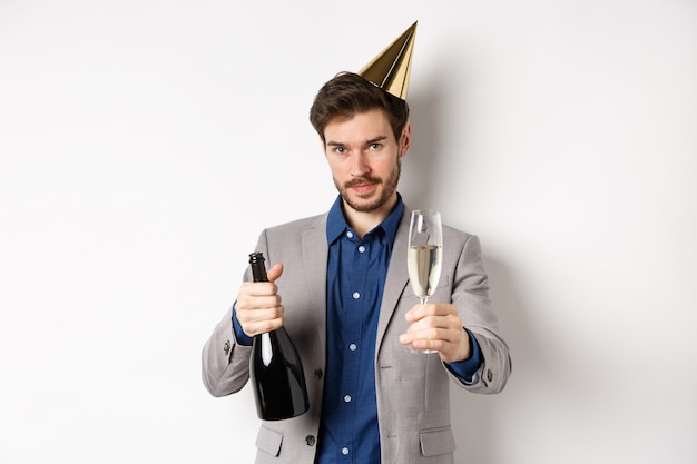 Concepto de celebración y vacaciones. Hombre guapo en traje y sombrero de cumpleaños dando copa de champán