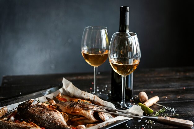 Concepto de cena con dos copas de vino blanco, pescado al horno.