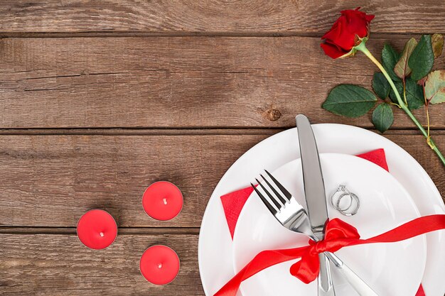 Concepto de cena romántica. Día de San Valentín o fondo de propuesta. Vista superior de la mesa de madera del restaurante con corazón y rosa con cubiertos en el plato. Copie el espacio en madera rústica