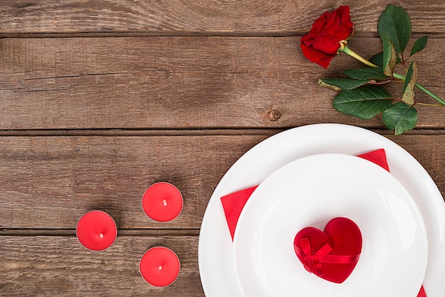 Concepto de cena romántica. Día de San Valentín o fondo de propuesta. Vista superior de la mesa de madera del restaurante con corazón y rosa con cubiertos en el plato. Copie el espacio en madera rústica