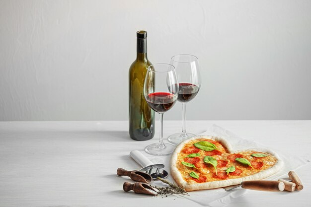 Concepto de cena romántica para dos con vino tinto y pizza en forma de corazón. cena para el dia de san valentin