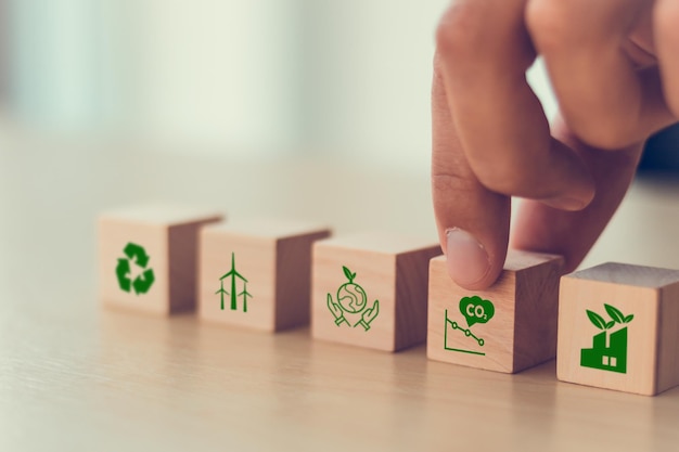 Concepto de cero emisiones netas y neutras en carbono Objetivo de emisiones netas cero de gases de efecto invernadero Estrategia a largo plazo neutra en el clima Coloca a mano cubos de madera con icono de disminución de las emisiones de carbono e icono verde Bandera verde