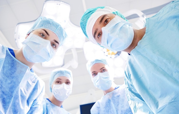 concepto de cirugía, medicina y personas - grupo de cirujanos en el quirófano del hospital mirando a la cámara