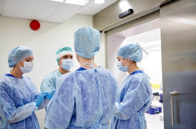 Concepto de cirugía, medicina y personas - grupo de cirujanos en la sala de operaciones en el hospital hablando y preparándose para la operación