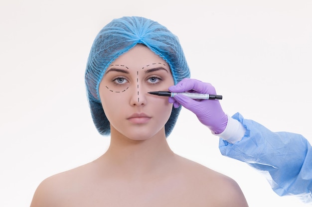 Concepto de cirugía plástica Doctor dibujando marcas en el rostro femenino contra el fondo blanco.