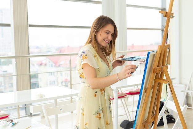 Foto concepto de clase de arte, dibujo y creatividad: estudiante sentada frente a un caballete con paleta y pincel
