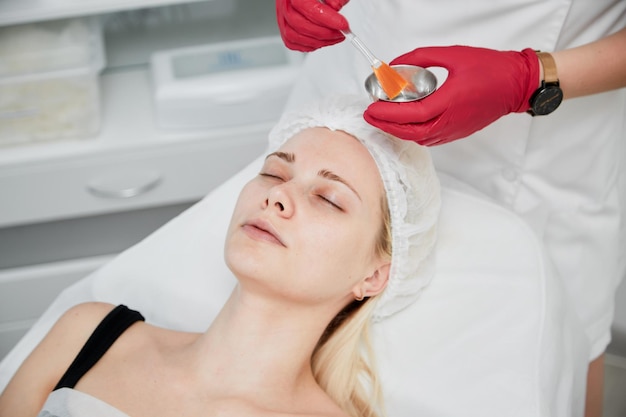 Concepto de clínica de belleza Mujer joven que obtiene un procedimiento facial profesional Cosmetóloga de retrato aplicando máscara en la cara del cliente en el salón de spa Centro de bienestar Ocupación de atención médica