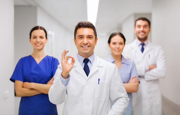 concepto de clínica, profesión, personas, atención de la salud y medicina - grupo de médicos felices o médicos en el pasillo del hospital que muestran el signo de la mano ok