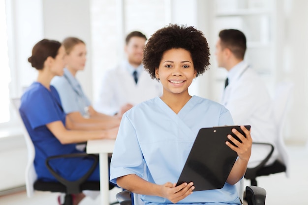 concepto de clínica, profesión, personas y medicina - doctora o enfermera feliz con portapapeles sobre un grupo de médicos reunidos en el hospital