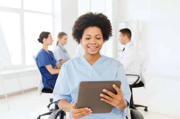 concepto de clínica, profesión, personas y medicina - feliz doctora o enfermera afroamericana con computadora de tablet pc sobre un grupo de médicos reunidos en el hospital