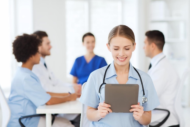 concepto de clínica, profesión, personas y medicina - feliz doctora con tablet pc sobre un grupo de médicos reunidos en el hospital