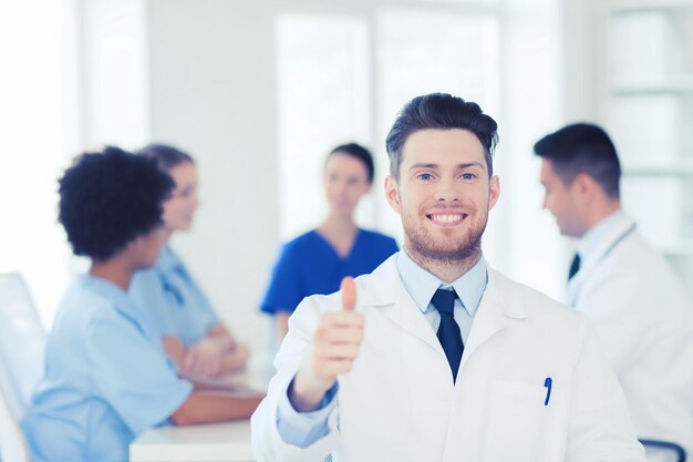 concepto de clínica, profesión, personas y medicina - médico varón feliz sobre un grupo de médicos reunidos en el hospital mostrando gesto de aprobación