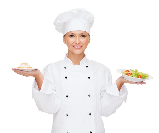 concepto de cocina y comida - chef sonriente, cocinera o panadera con ensalada y pastel en platos