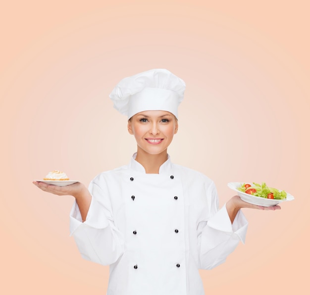 concepto de cocina y comida - chef sonriente, cocinera o panadera con ensalada y pastel en platos