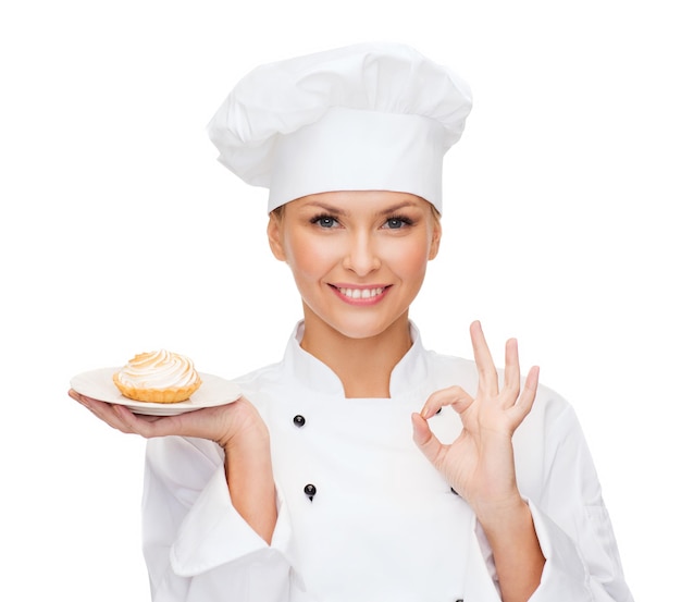 concepto de cocina y comida - chef sonriente, cocinera o panadera con pastel en el plato y signo ok