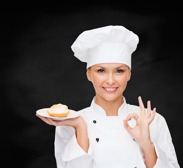 concepto de cocina y comida - chef sonriente, cocinera o panadera con pastel en el plato y signo ok