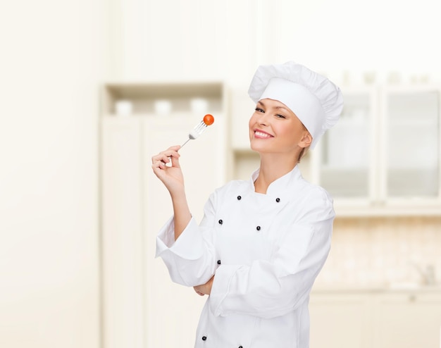 concepto de cocina y comida - chef sonriente, cocinera o panadera con tenedor y tomate