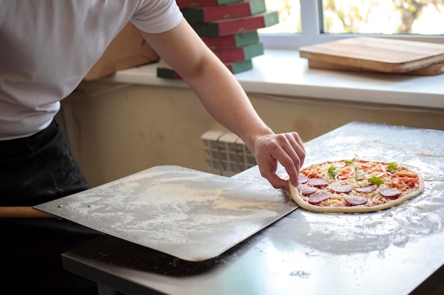 Foto el concepto de cocina culinaria y de personas - cocinar o hornear a mano con pizza en la cáscara en la pizzería