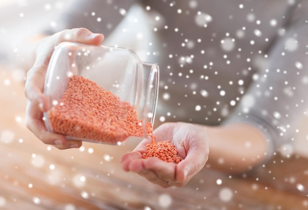 concepto de cocina, gente y hogar - cierre de una mujer vaciando un frasco con lentejas rojas en la cocina