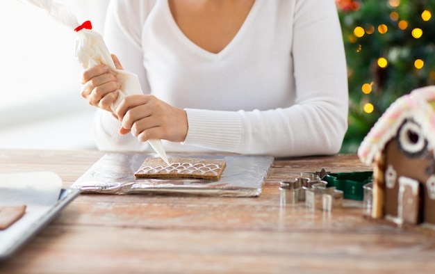 concepto de cocina, gente, navidad y decoración - cerca de una mujer feliz haciendo casas de pan de jengibre en casa