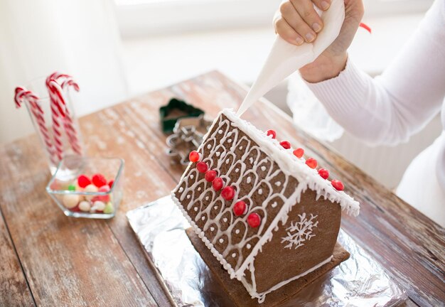 concepto de cocina, gente, navidad y decoración - cerca de una mujer feliz haciendo casas de pan de jengibre en casa